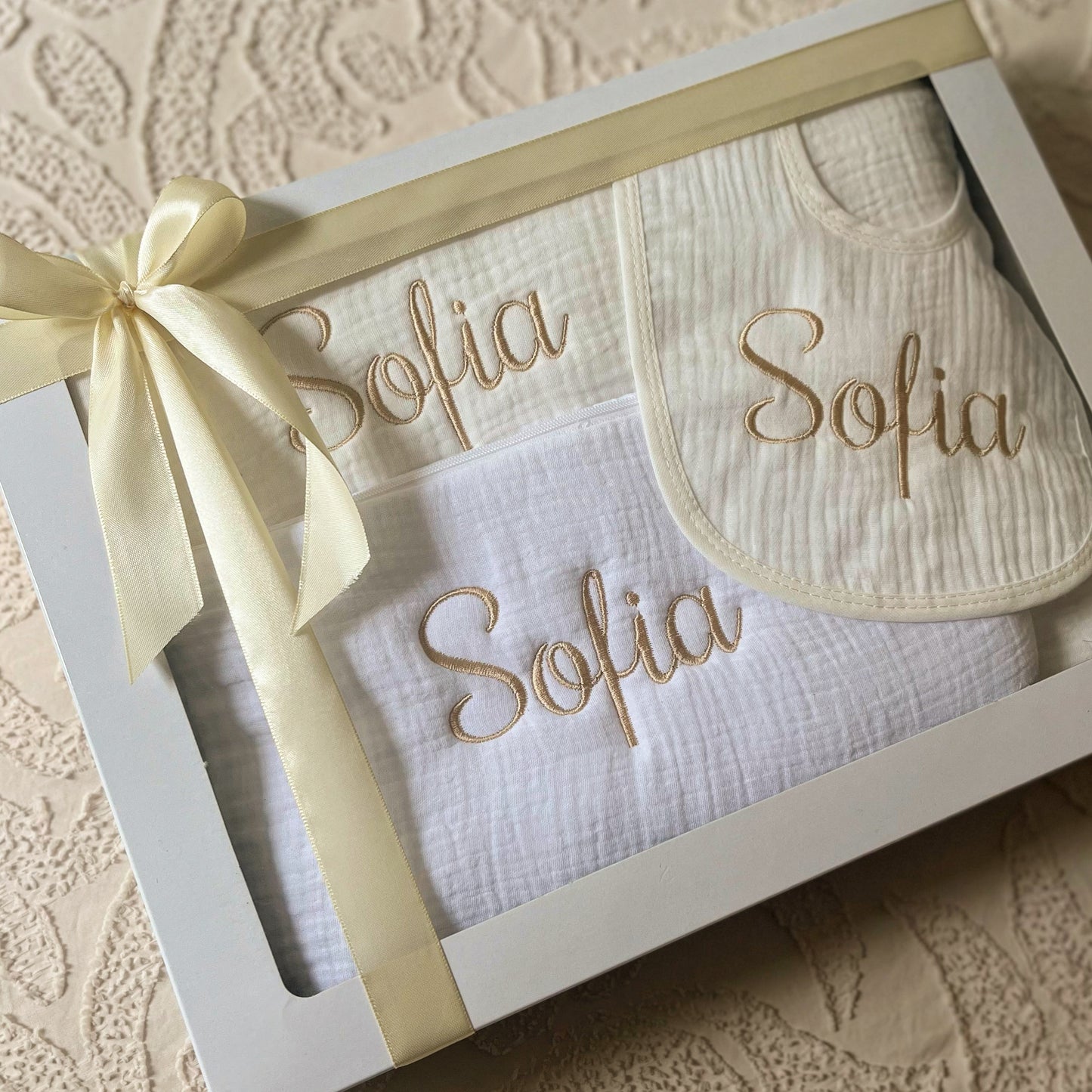 
Coffret naissance bébé en gaze de coton comprenant couverture, trousse de toilette et bavoir personnalisés au prénom, cadeau doux et pratique.