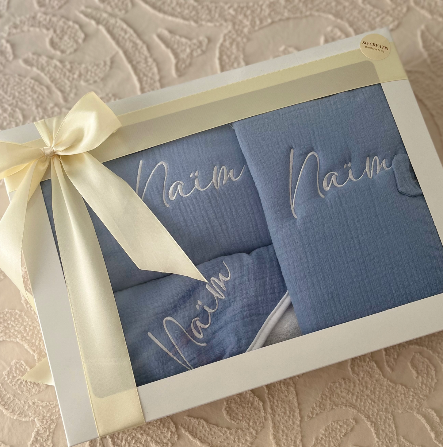 Coffret naissance bébé comprenant couverture moelleuse, cape de bain douce et protège carnet de santé élégant, parfait comme cadeau pratique et raffiné.